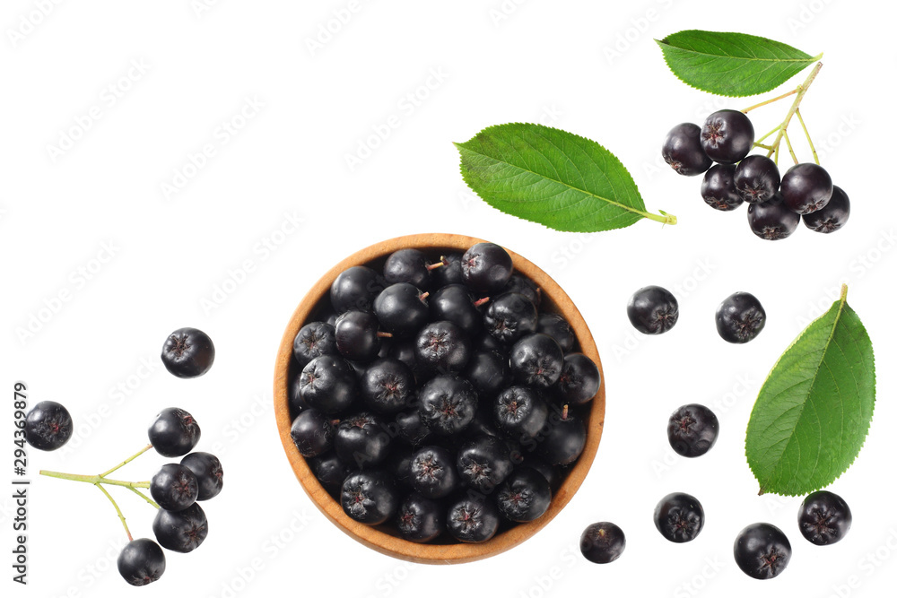 Chokeberry in wooden bowl with green leaves isolated on white background. Black aronia. Top view. Chokeberry in wooden bowl with green leaves isolated on white background. Black aronia. Top view.