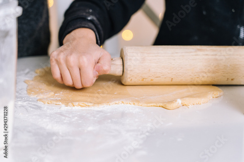 Detail of young kids baking Christmas gingerbread cookies in house kitchen on winter day. Child with rolling pin baking cookies. Baking and cooking with children for Christmas at home.Selective focus