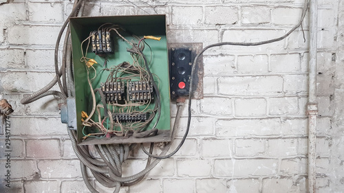 Old electrical panel on the wall of the house. Electric cables stick out from the electric panel on the white brick wall of the old house.