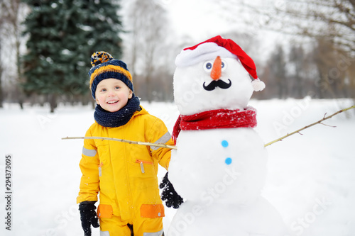Little boy playing with funny snowman. Active outdoors leisure with children in winter.