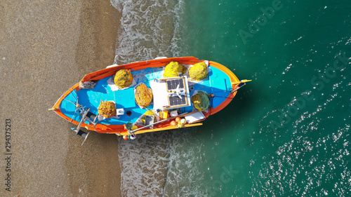 Aerial top view photo of red traditional wooden fishing boat in Aegean island destination beach with emerald sea
