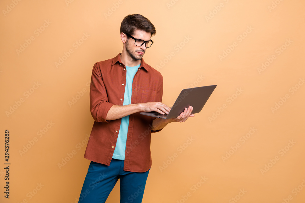 Portrait of his he nice attractive serious successful smart clever focused concentrated brunette guy holding in hands laptop browsing isolated over beige color pastel background Portrait of his he nice attractive serious successful smart clever focused concentrated brunette guy holding in hands laptop browsing isolated over beige color pastel background