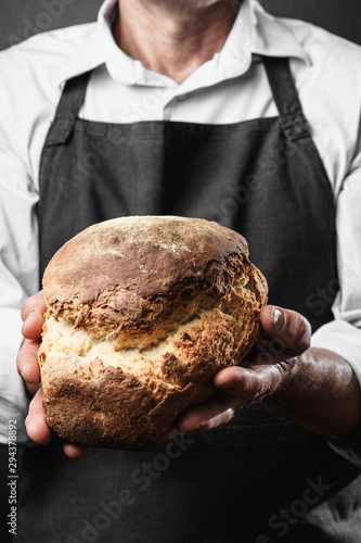 man with fresh bread in his hands, baker in apron and shirt givi photo