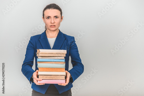 Young teacher carrying a stack of heavy books, frowning her face.