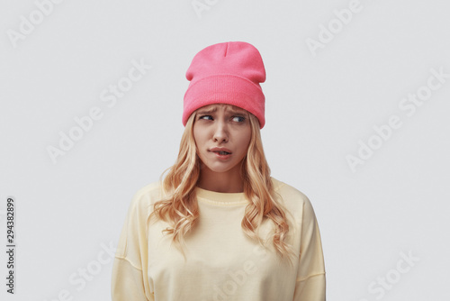 Photos Sad young woman making a face and looking away while standing against grey backg
