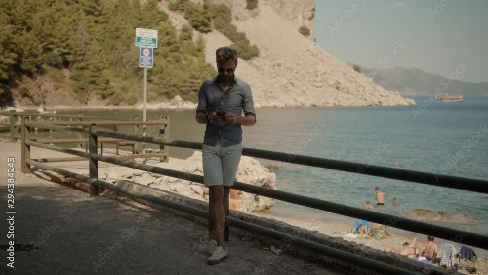 Male Chatting With Friends.Man Using Mobile Phone On Vacation In Sunny Day.Man Having Chat On Smartphone At Mediterranean Beach.Relaxed Man Looking And Texting On Mobile Phone In Vocation Near Sea. Male Chatting With Friends.Man Using Mobile Phone On Vacation In Sunny Day.Man Having Chat On Smartphone At Mediterranean Beach.Relaxed Man Looking And Texting On Mobile Phone In Vocation Near Sea.
