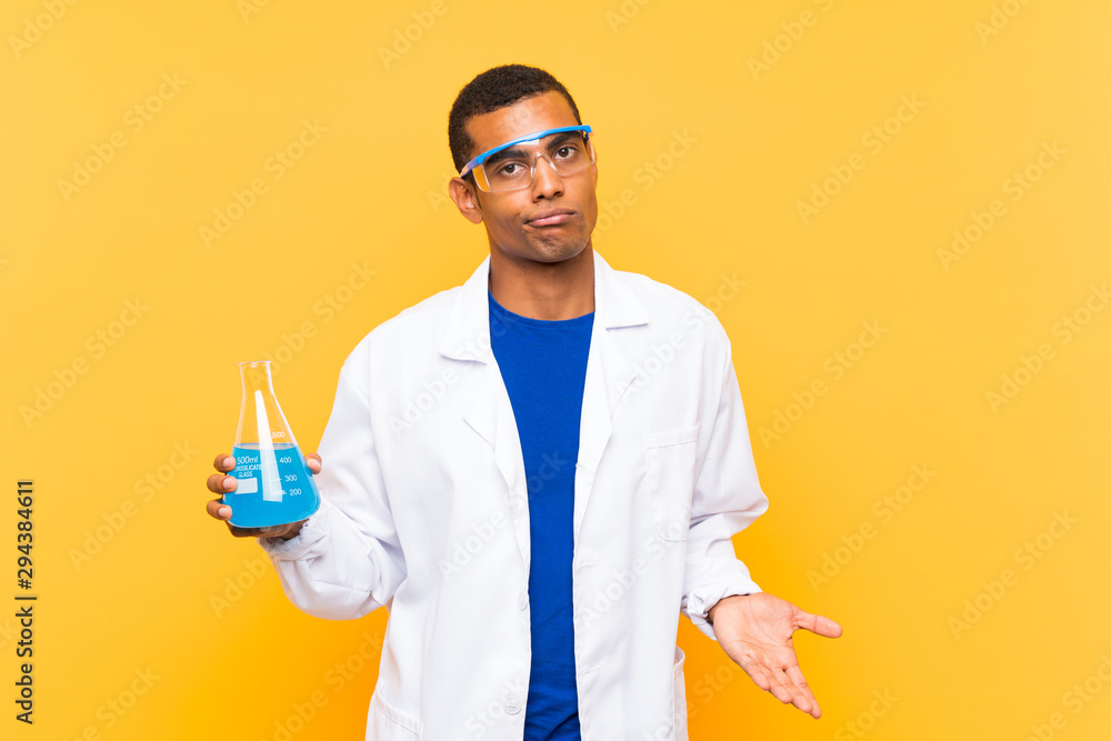 Scientific man holding a laboratory flask over isolated background making doubts gesture while lifting the shoulders Scientific man holding a laboratory flask over isolated background making doubts gesture while lifting the shoulders