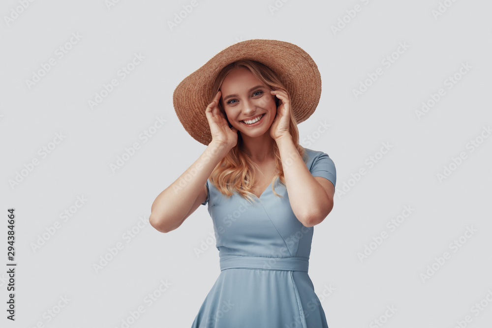 Attractive young woman smiling and looking at camera while standing against grey background Attractive young woman smiling and looking at camera while standing against grey background