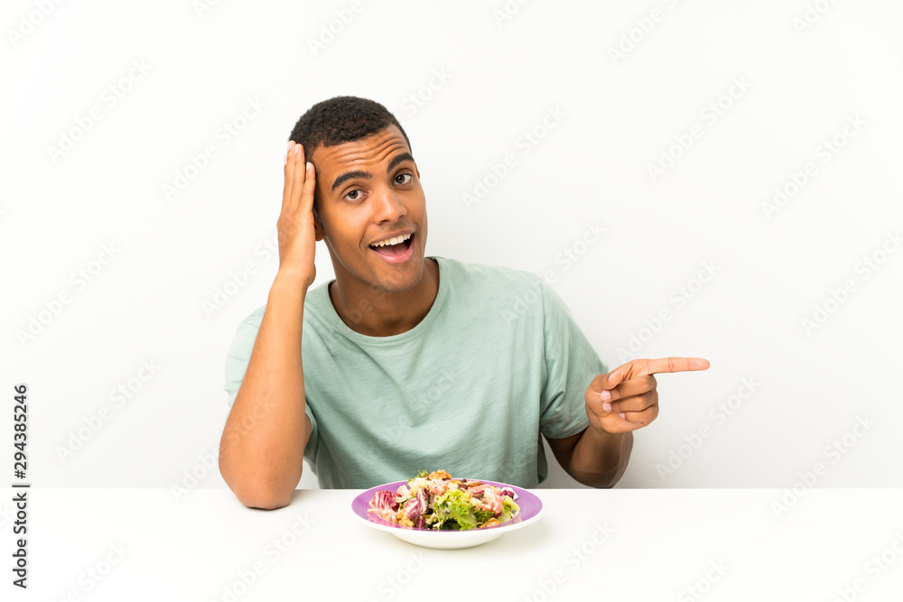 Young handsome man with salad in a table surprised and pointing finger to the side Young handsome man with salad in a table surprised and pointing finger to the side