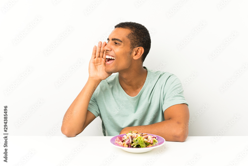 Young handsome man with salad in a table shouting with mouth wide open Young handsome man with salad in a table shouting with mouth wide open