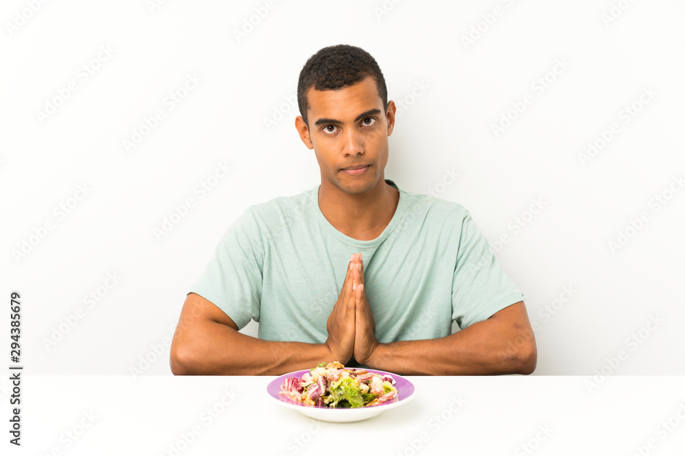 Young handsome man with salad in a table pleading