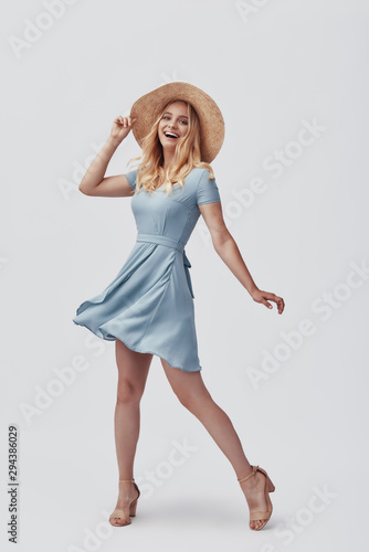 Full length of attractive young woman looking at camera and smiling while standing against grey background