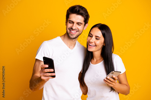 Photo of two people holding telephones watching funny humorous video wear casual clothes isolated yellow color background