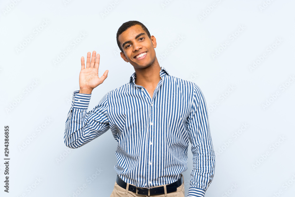 Young handsome brunette man over isolated blue background saluting with hand with happy expression Young handsome brunette man over isolated blue background saluting with hand with happy expression