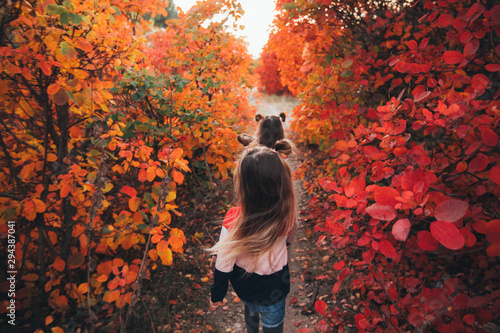 Twin blondes walk and have fun in the autumn forest among the red trees.