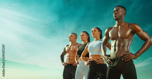 Group of four young sportsmens women and men, fit athletes are standing on the sky background before run. Healthy lifestyle and sport. Friends in black and white sportswear. Fitness concept.