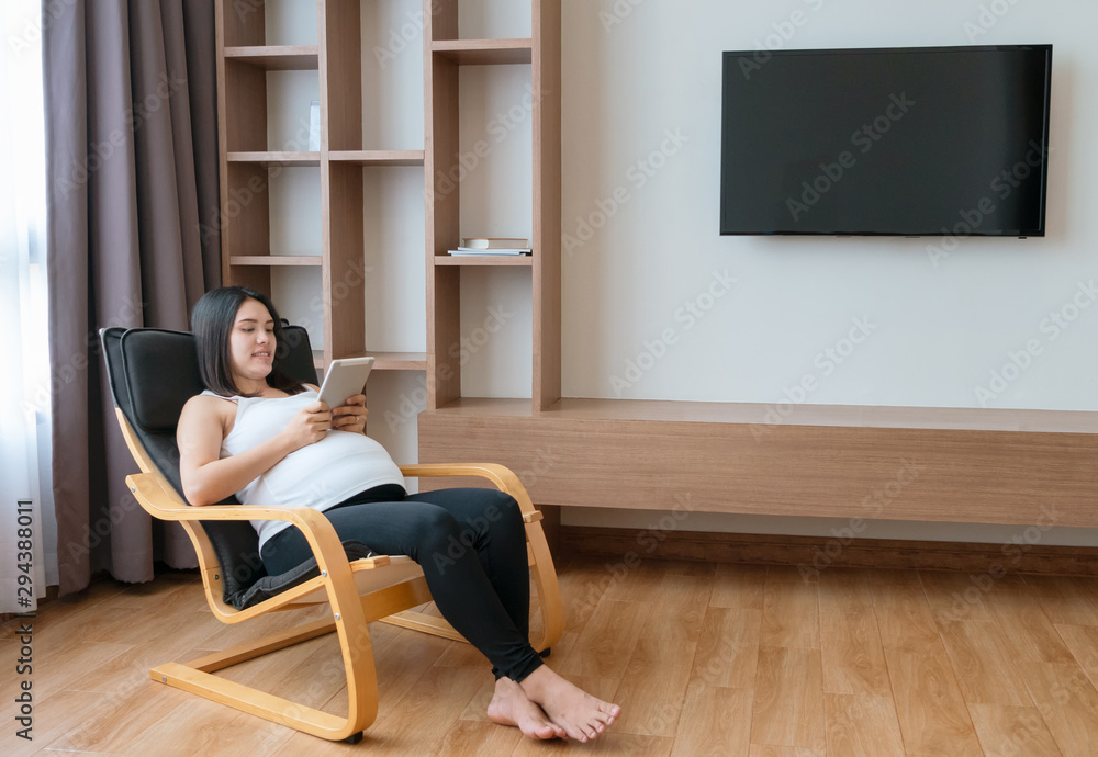 Pregnant woman resting on modern rocking-chair with tablet computer in living room. Pregnant woman resting on modern rocking-chair with tablet computer in living room.