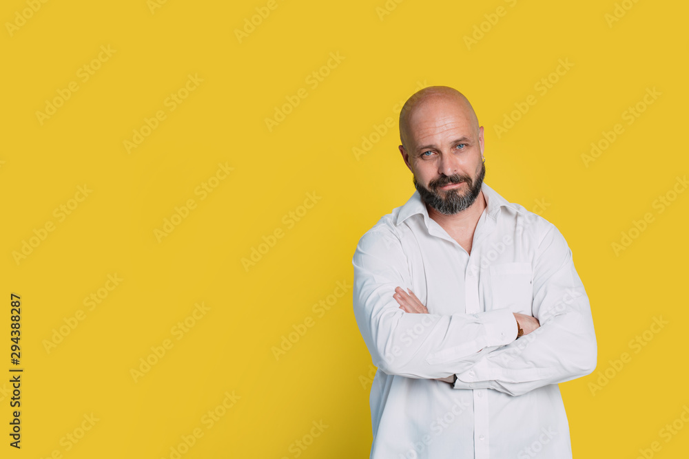 Serious middle-aged man with folded arms and a deadpan expression posing in front of a yellow background with copy space Serious middle-aged man with folded arms and a deadpan expression posing in front of a yellow background with copy space