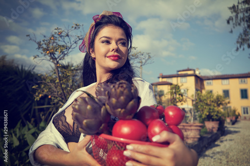 La dolce vita lifestyle. An Italian woman is carrying a basket with vegetables. House and garden in the background