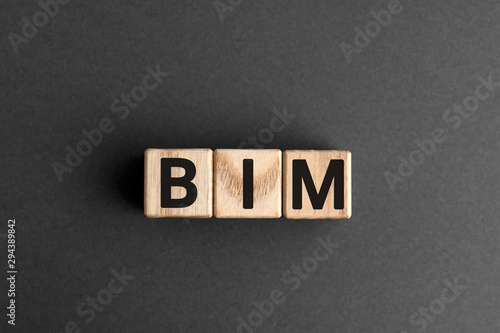 BIM - acronym from wooden blocks with letters, abbreviation BIM Building Information Modeling concept, gray background
