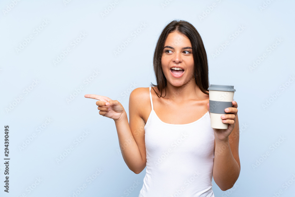 Young woman holding a take away coffee over isolated blue background surprised and pointing finger to the side Young woman holding a take away coffee over isolated blue background surprised and pointing finger to the side