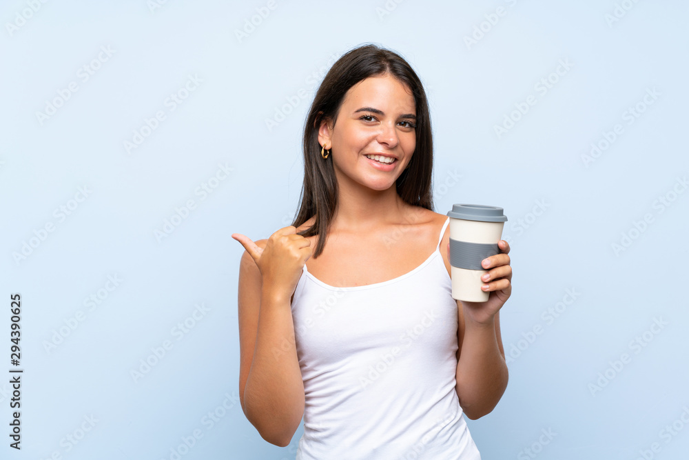 Young woman holding a take away coffee over isolated blue background pointing to the side to present a product Young woman holding a take away coffee over isolated blue background pointing to the side to present a product