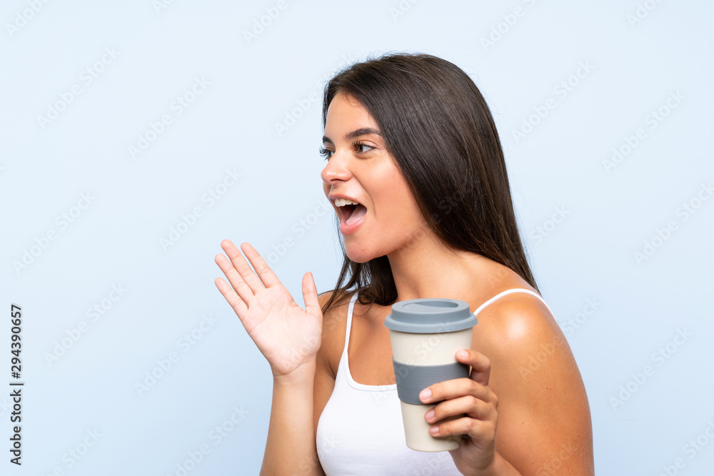 Young woman holding a take away coffee over isolated blue background shouting with mouth wide open Young woman holding a take away coffee over isolated blue background shouting with mouth wide open