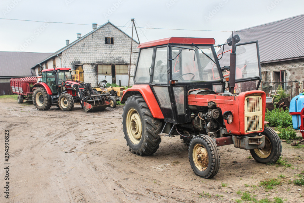 Red tractors and agricultural equipment in the courtyard of a dairy farm. A cowshed in the background.Close up. Podlasie, Poland. Red tractors and agricultural equipment in the courtyard of a dairy farm. A cowshed in the background.Close up. Podlasie, Poland.