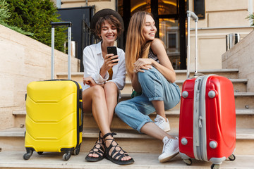 Photo of two smiling caucasian women using mobile phone while sitting
