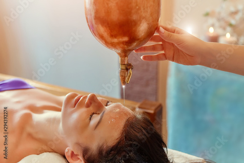 ayurveda massage alternative healing therapy.beautiful caucasian female getting shirodhara treatment lying on a wooden table in India salon.