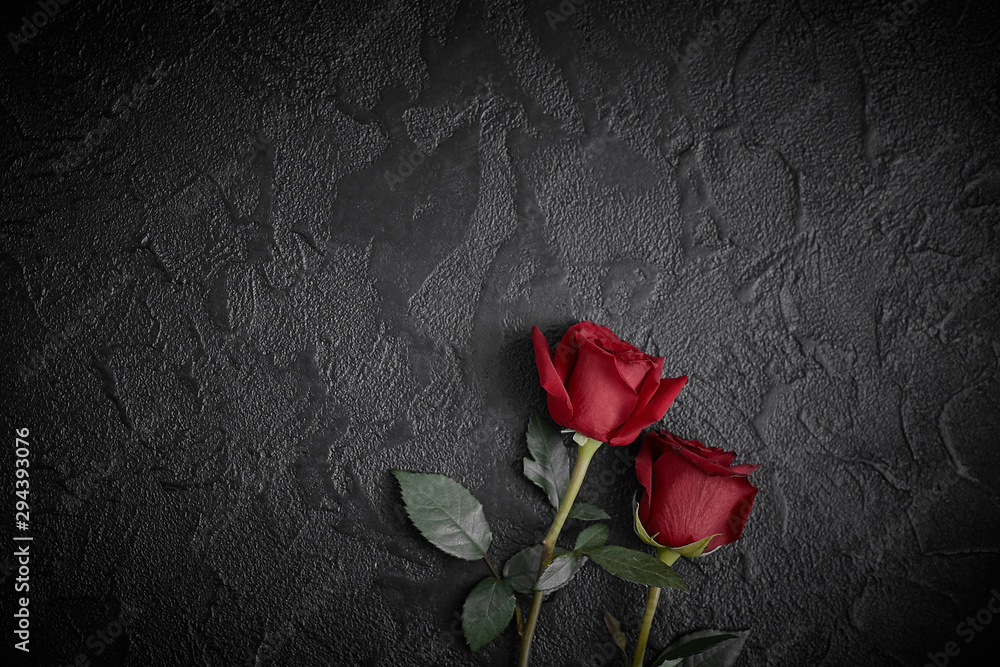 Red roses are placed on a black textured background. A sign of condolence, sympathy loss. Space for your text.