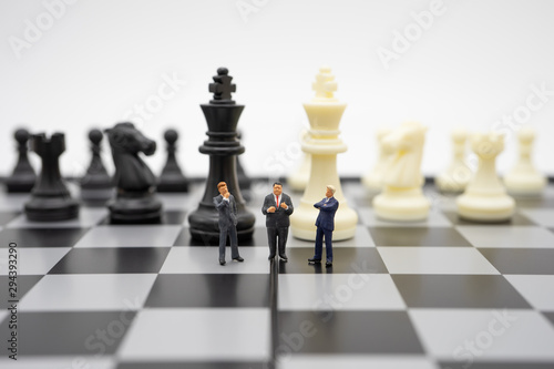 Fototapeta Miniature people businessmen standing on a chessboard with a chess piece on the back Negotiating in business
