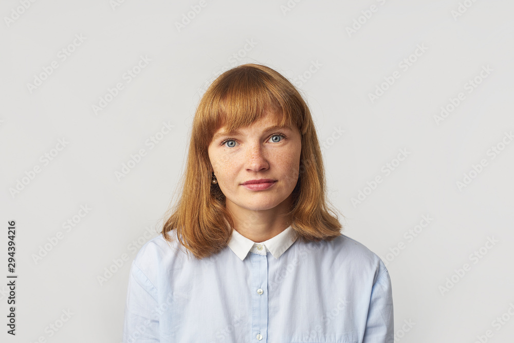 Headshot of young female model with ginger hair and freckles dressed in blue shirt looking at the camera. Isolated on white background Headshot of young female model with ginger hair and freckles dressed in blue shirt looking at the camera. Isolated on white background