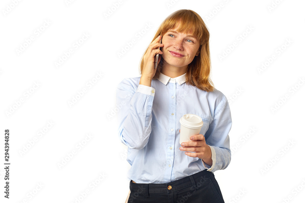 Portrait of young redheaded woman with freckles and bang talking on a phone smiling and holding a cup of coffee in her hands Portrait of young redheaded woman with freckles and bang talking on a phone smiling and holding a cup of coffee in her hands