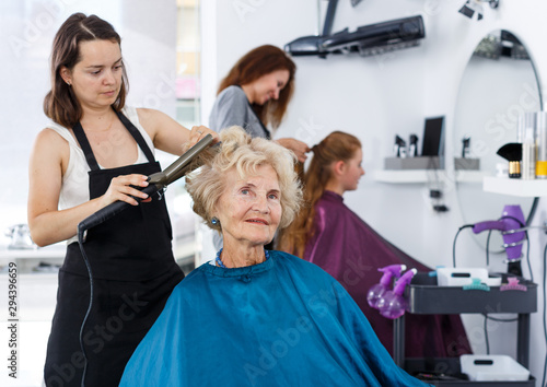Hairdresser curling hair of elderly female