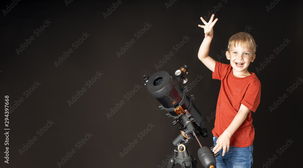 A little boy is standing with a large telescope and pointing his finger to the top.