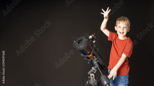 A little boy is standing with a large telescope and pointing his finger to the top.