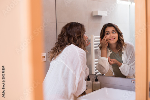 Beautiful woman in the bathroom moisturizing her skin