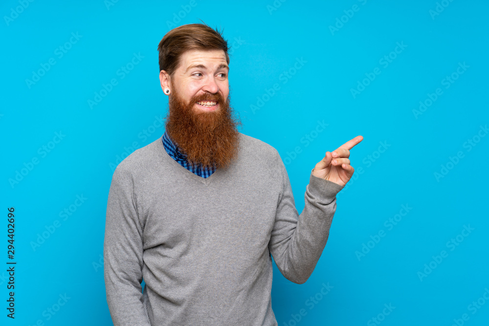 Redhead man with long beard over isolated blue background pointing finger to the side Redhead man with long beard over isolated blue background pointing finger to the side
