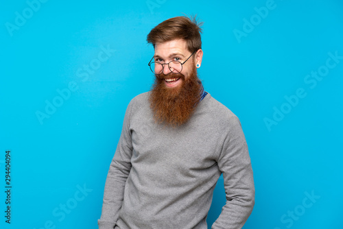 Redhead man with long beard over isolated blue background with glasses and surprised © luismolinero