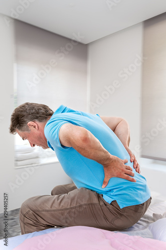 Senior male suffering sharp back pain, sick person getting up from bed, after rest