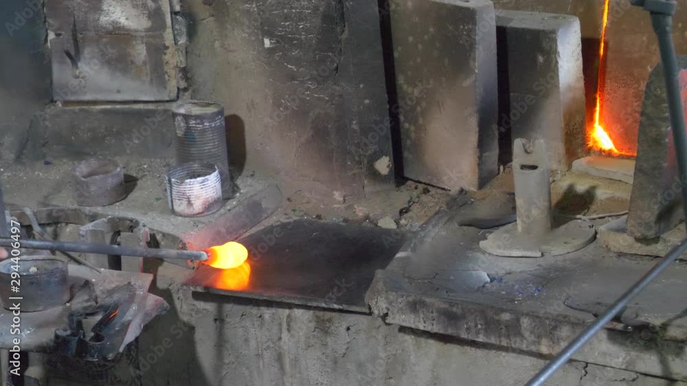Skilled glassblower and artist forms art from red hot molten glass heated in a furnace Skilled glassblower and artist forms art from red hot molten glass heated in a furnace