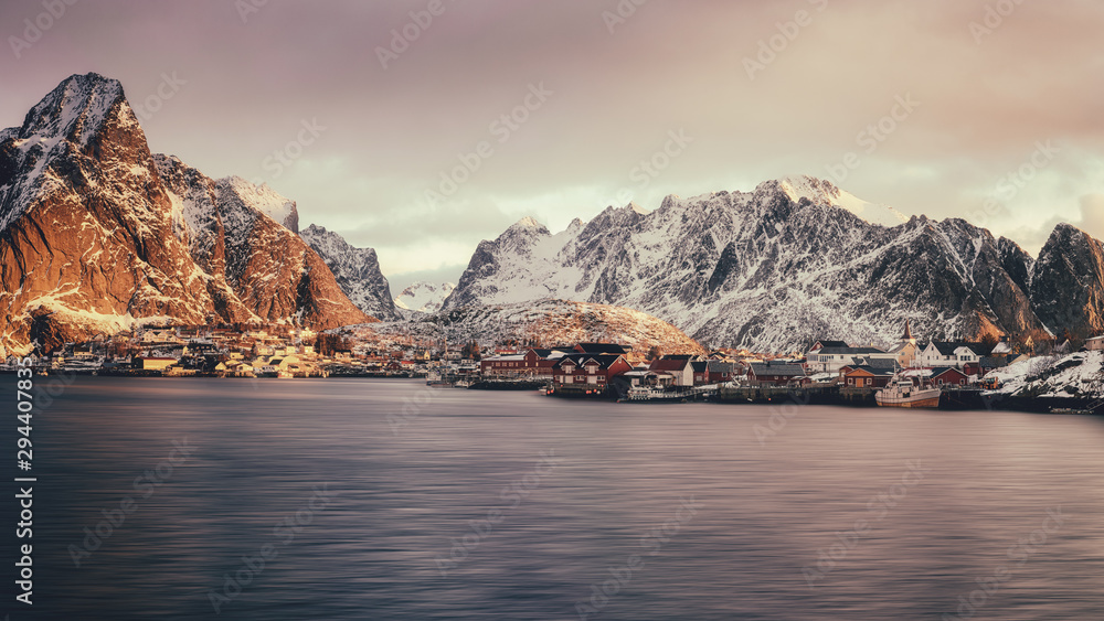 Scenic view of Reine, famous fishing village at sunrise, Lofoten Islands, Norway. Amazing winter landscape with rocky mountains, traditional rorbues, water and dramatic cloudy sky, travel background