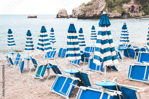 Clossed umbrellas with blue line. The end of the summer season. Closed umbrellas with blue and white lines and sunbeds on the beach. © Struzhkova Ilona