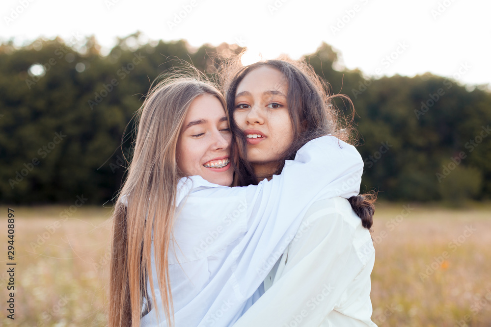 Fototapeta premium Two young women in white shirts hugging outdoors. Best friends