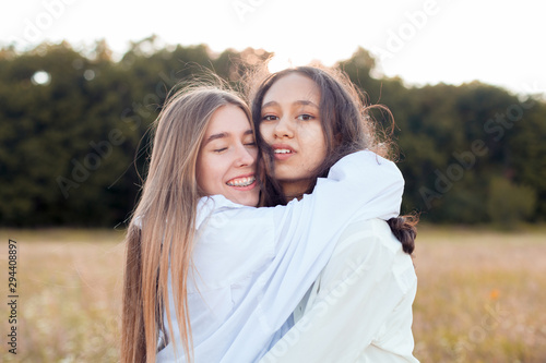 Two young women in white shirts hugging outdoors. Best friends