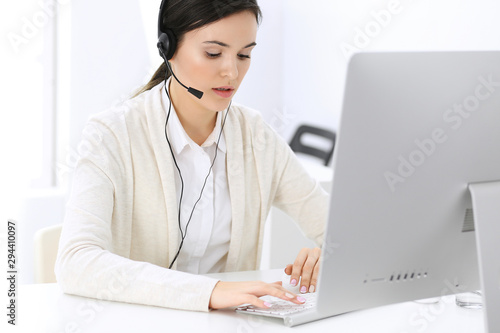 Call center. Beautiful woman receptionist sitting in headset at customer service office. Group of operators at work. Business concept