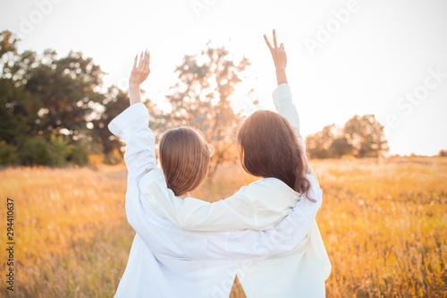 Two girls in white shirts looking on the sunset and rise up hands. Best friends