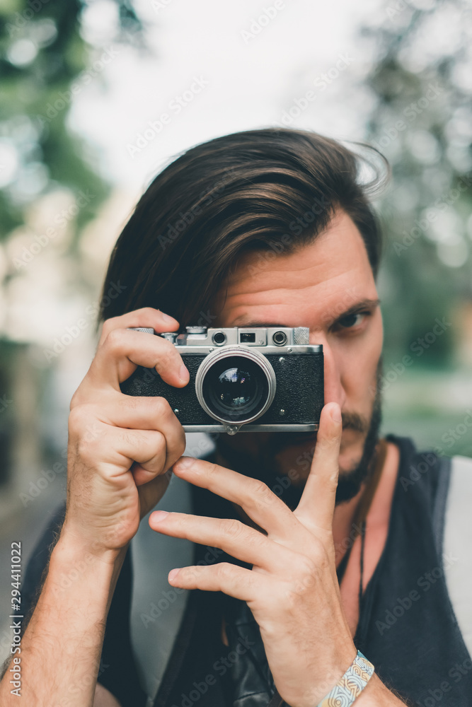 Young handsome beard man in white shirt and trousers makes beautiful pictures on film retro camera, stylishly dressed, photographer,outdoor portrait, close up,brutal, tattoo, street photo,photographer