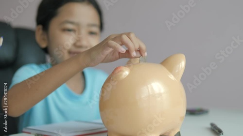 Little Asian girl puttinwg the coin into piggy bank and smile with happiness for money saving to wealthness in the future of education concept select focus shallow depth of field photo